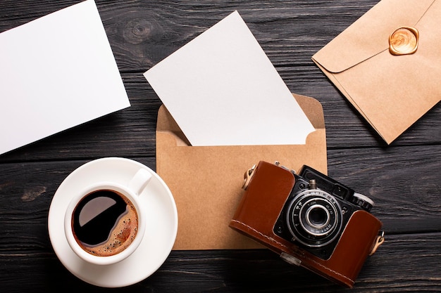 Een envelop met een plek voor een inscriptie, een mooie camera en een kopje koffie met schuim op een zwarte houten achtergrond