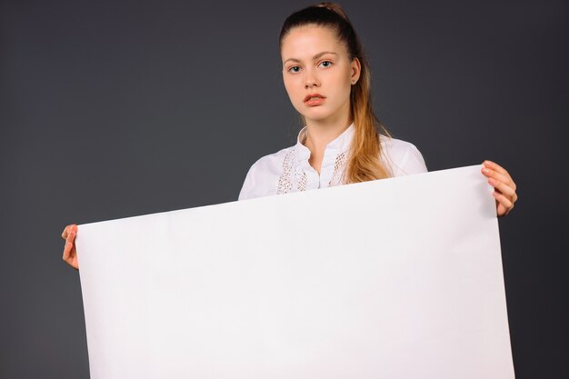 Foto een ernstige jonge bedrijfsvrouw houdt in haar wapen een lege witte banner