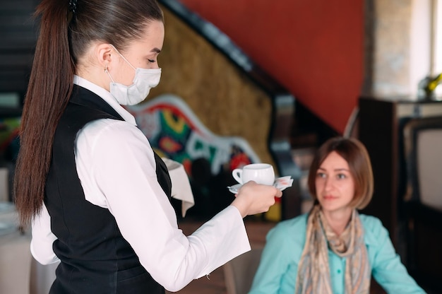 Een europees ogende ober met een medisch masker serveert koffie.