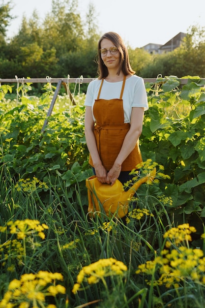 Een europese vrouw in een oranje schort is komkommers en erwten aan het oogsten in haar tuin een vrouwelijke tuinman