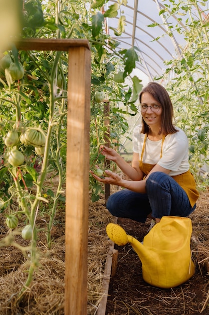 Een Europese vrouw met een gele gieter geeft groenten en fruit in haar tuin water