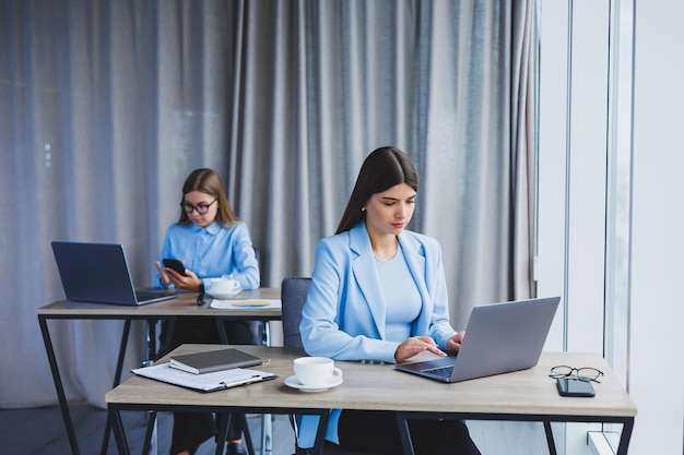 Een europese zakenvrouw praat op een mobiele telefoon terwijl haar europese collega op de achtergrond werkt concept van moderne succesvolle vrouwen jonge meisjes zitten aan bureaus in zonnig kantoor