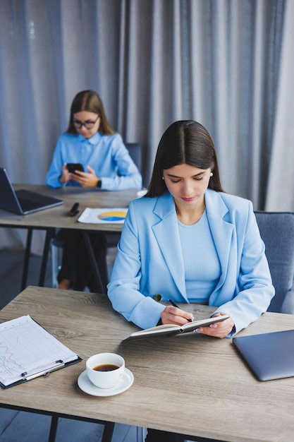 Een Europese zakenvrouw praat op een mobiele telefoon terwijl haar Europese collega op de achtergrond werkt Concept van moderne succesvolle vrouwen Jonge meisjes zitten aan bureaus in zonnig kantoor