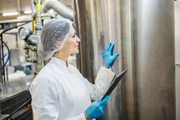 Een expert in de melkverwerkingsfabriek houdt de melktank in de gaten terwijl ze een tablet in haar handen houdt