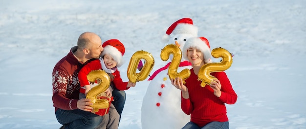 Een familie houdt de cijfers van het komende nieuwe jaar naast een sneeuwpop op zonnige kerstdag