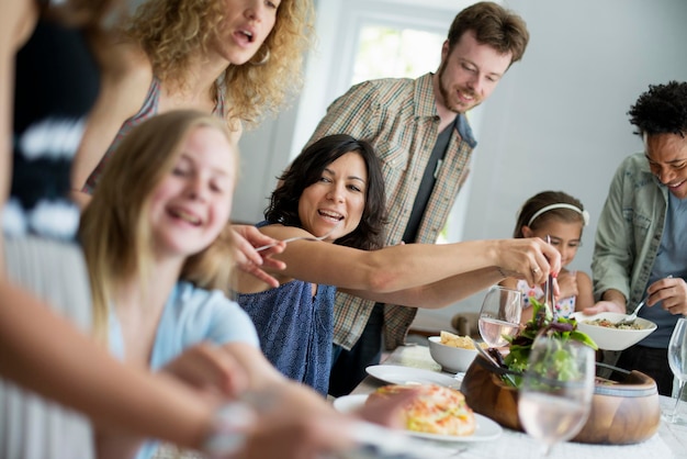 Een familiebijeenkomst voor een maaltijd Volwassenen en kinderen rond een tafel