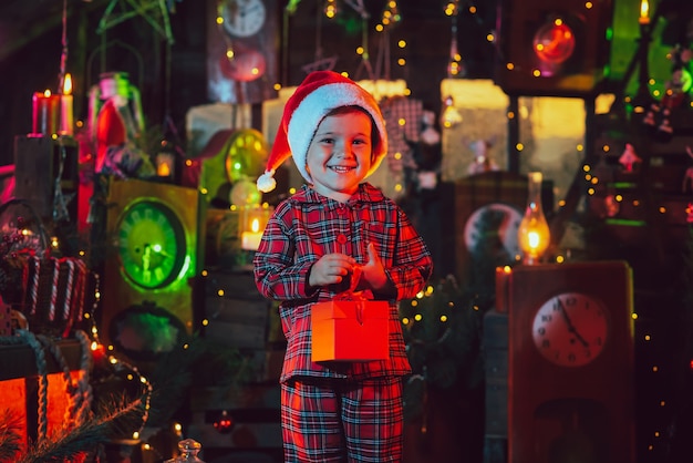 Een fantastische kerstsfeer. Een kindjongen houdt een doos met een geschenk in zijn handen in de nieuwjaarsversieringen. foto voor een ansichtkaart.