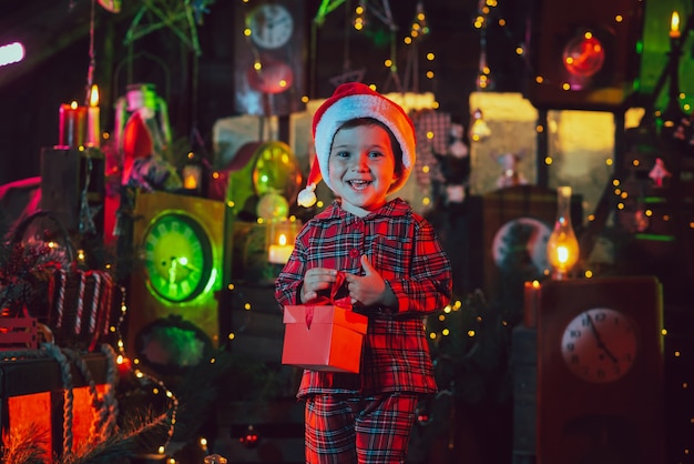 Een fantastische kerstsfeer. Een kindjongen houdt een doos met een geschenk in zijn handen in de nieuwjaarsversieringen. gekleurd licht. foto voor een ansichtkaart.