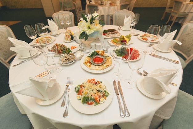 Een feestelijke tafel serveren met een variatie aan gerechten. Salades, vis, fruit, groenten, glazen, bestek op een lichte tafel.