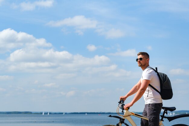 Een fietser met rugzak en bril rijdt op een mooie zonnige dag langs de zee op een fiets.