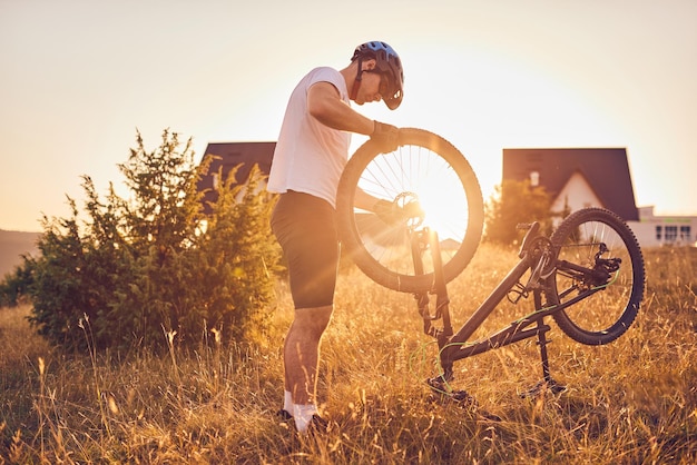 Een fietser repareert een fiets op een bosweg bij zonsondergang. Foto van hoge kwaliteit