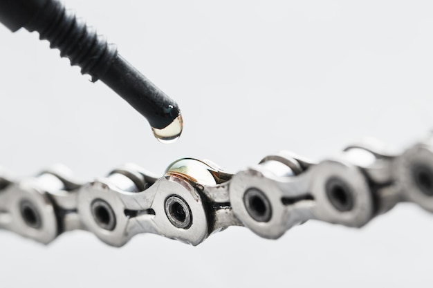 Een fietsketting invetten met een druppel gouden olie close-up op een grijze achtergrond