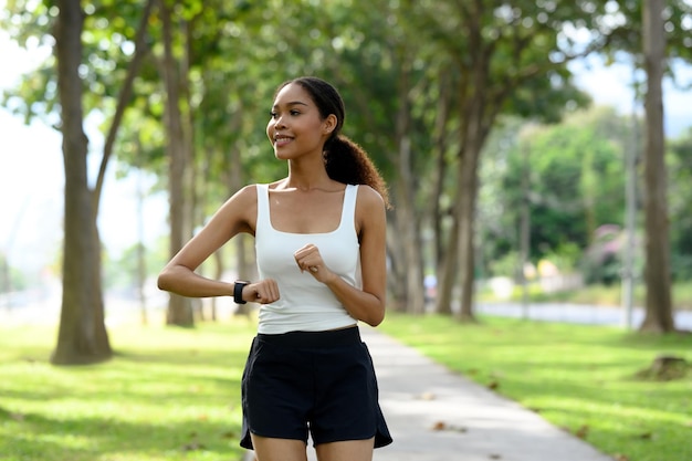 Een fit jonge Afrikaanse vrouw houdt haar oefenvorderingen bij op een smartwatch terwijl ze buiten joggt