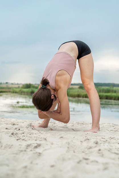 een fitnessinstructeur toont hoe je stretching-oefeningen op de zandkust van het meer correct kunt uitvoeren Workout in de natuur