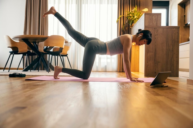 Een fitte Japanse vrouw beoefent thuis fitness oefeningen op een online les.