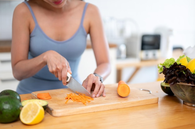 Een fitte vrouw in gymkleding snijdt wortels op een snijplank en bereidt haar gezonde ontbijt voor