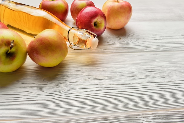 Een fles appelsap en appels op een witte houten tafel met kopieerruimte. Een fles appelciderazijn close-up.