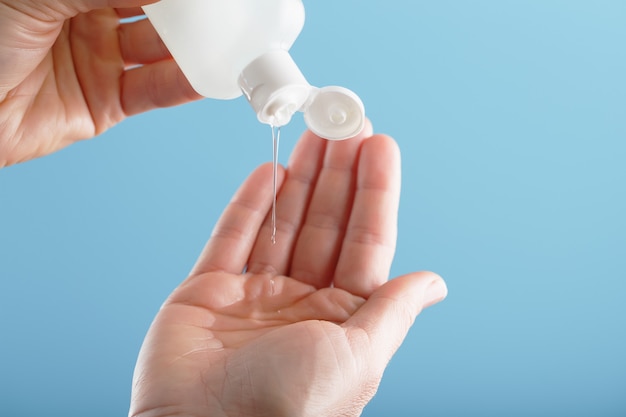 Een fles desinfecterende gel in uw handen op een blauwe achtergrond. Antiseptische behandeling van handen door bacteriën Sanitizer.