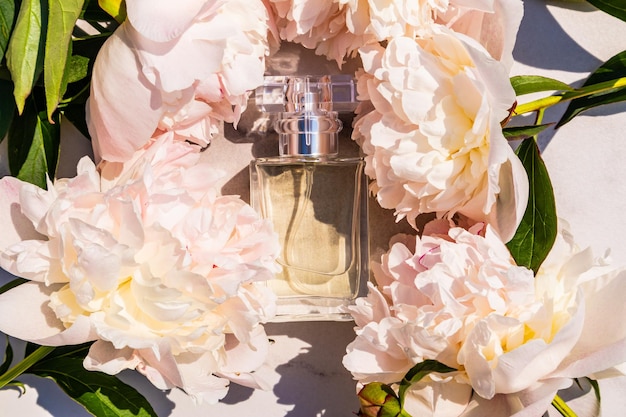 Een fles elegant bloemenparfum of toiletwater tussen verse delicate pioenrozen op een witte marmeren achtergrond aromapresentatie natuurlijk parfum