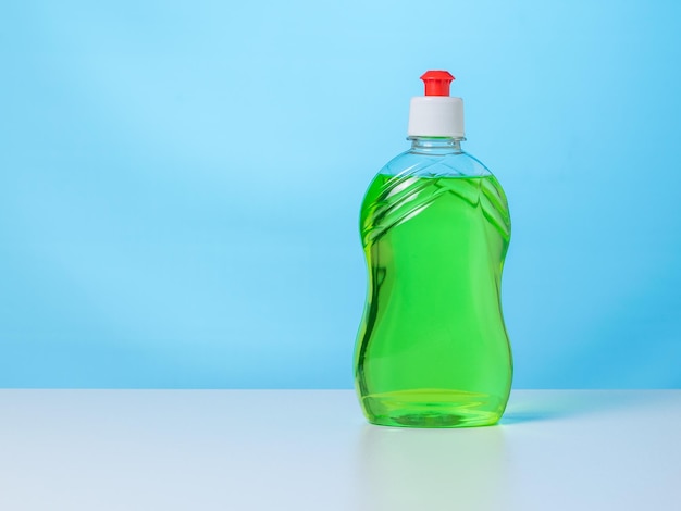 Een fles groene reinigingsgel op een witte tafel op een blauwe achtergrond