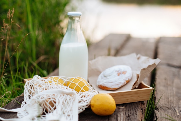 Een fles melk en een zakje met fruit op houten planken op het meer