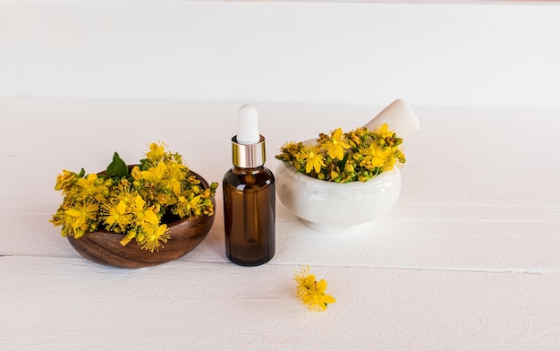 Een fles met gezichtsserum dat natuurlijke sint-janskruidolie geneest op een witte houten achtergrond met de bloemen van de alternatieve geneeswijze van de plant