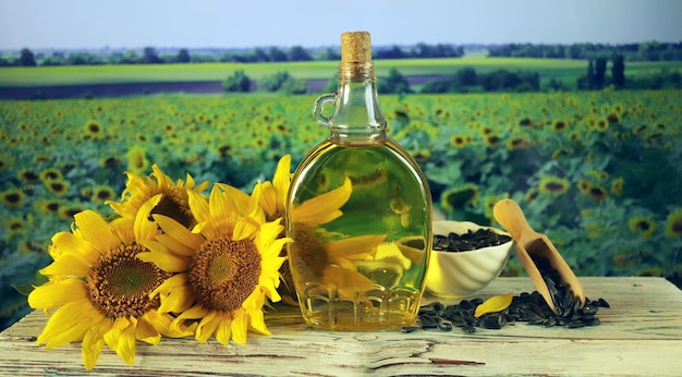 Een fles olie, verse zonnebloembloemen en zaden, tegen de achtergrond van een landschap