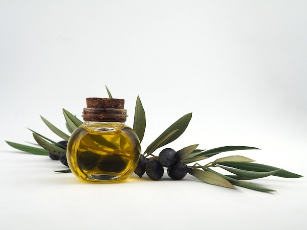 Een fles olijfolie op de achtergrond van een olijfboomtak met zwarte olijven en bladeren