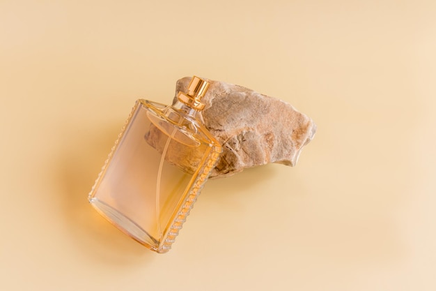 Een fles parfum of toiletwater gemaakt van helder glas ligt op een beige steen reclameconcept van parfum cosmetica pastel achtergrond