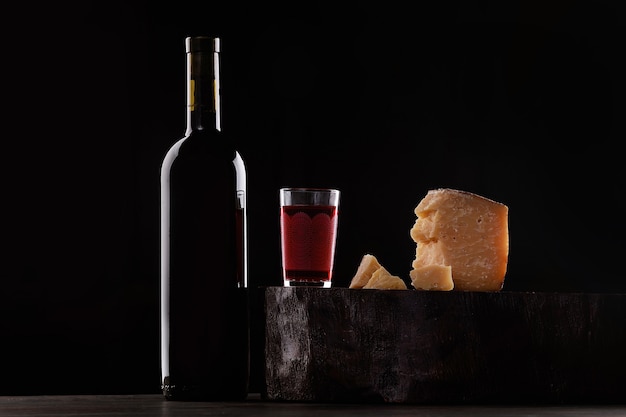 Een fles rode wijn en een glas rode wijn, een dure kaassoort met schimmel en druiven. op zwarte achtergrond. plaats voor logo.