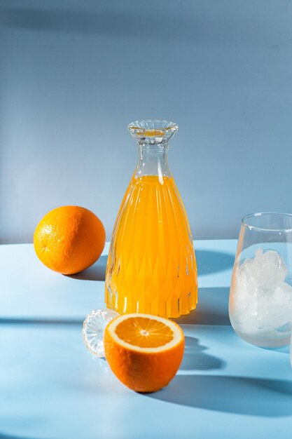 Foto een fles sinaasappelsap en een glas ijs op een blauwe tafel.