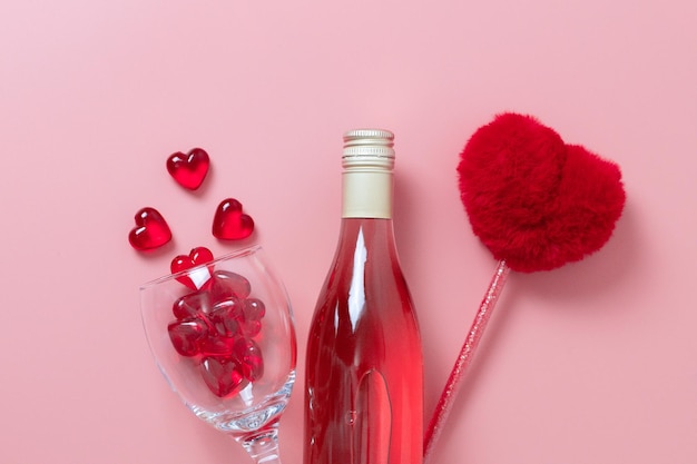 Een fles wijn een glas met glazen hartjes en een pen op roze