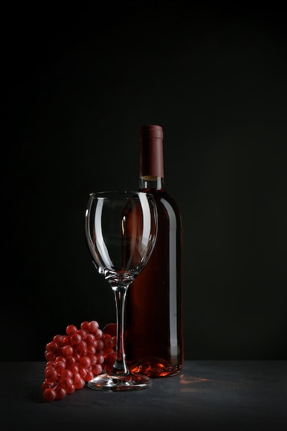 Een fles wijn en rode druiven, op grijs-zwarte achtergrond
