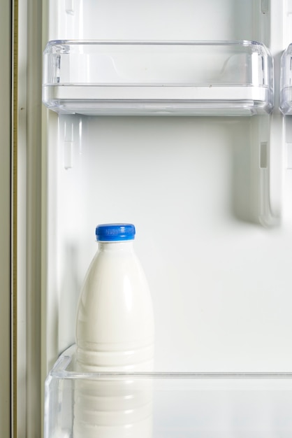 Een fles zure room in koelkastyoghurt in witte fles op plank van open lege koelkast gewicht l...