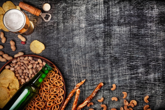 Een flesje bier op een bord met gezouten ookies pretzels, pistachenoten en chips op een zwart gekrast krijtbord