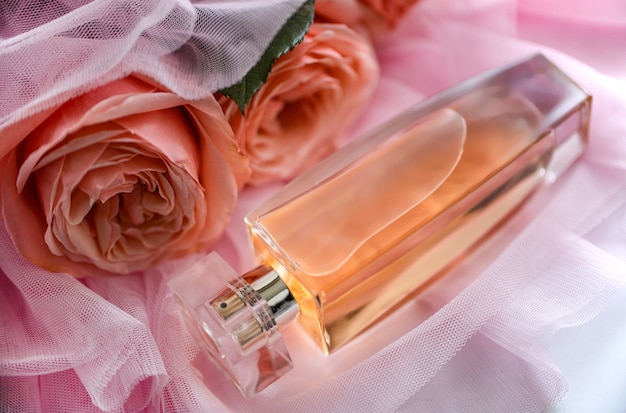 Foto een flesje parfum op een roze sluier met een roze roos vooraanzicht