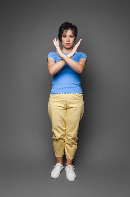 Een foto van een jonge, behoorlijk serieuze vrouw met gekruiste armen toont het verboden geen stop-symbool gemarkeerd tegen een grijze achtergrond