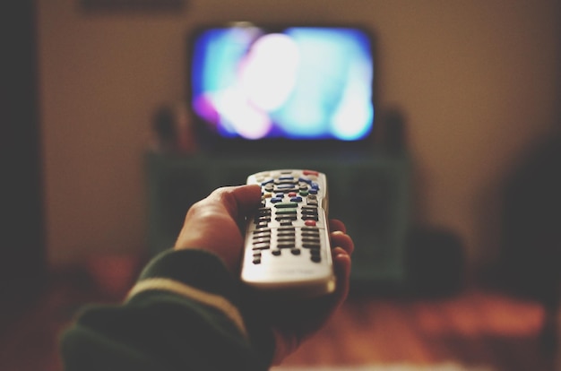 Een foto van een persoon met een afstandsbediening tegen de televisie thuis.