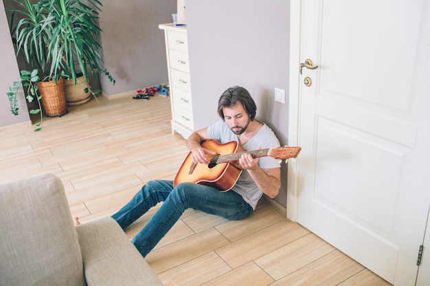 Een foto van man zittend op de vloer en gitaar spelen