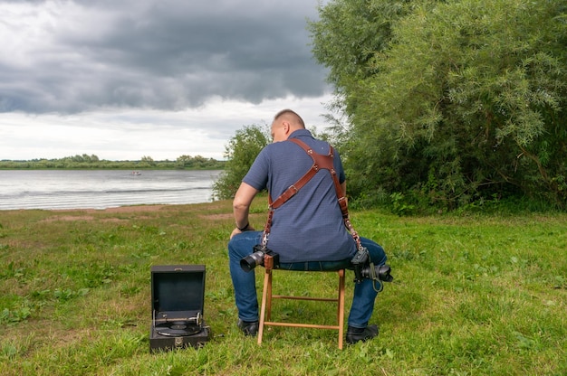 Een fotograaf met een camera zit in de zomer aan de oever van de rivier
