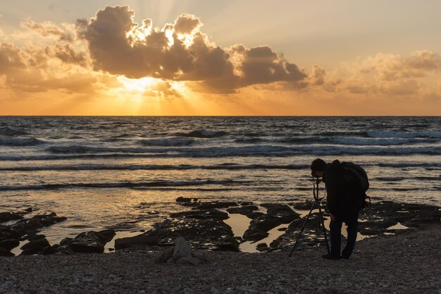Een fotograaf met een statief legt de zonsondergang vast op een strand bij Haifa