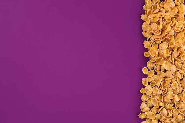 Een frame bekleed met cornflakes Cornflakes verspreid over een paarse achtergrond Ruimte kopiëren