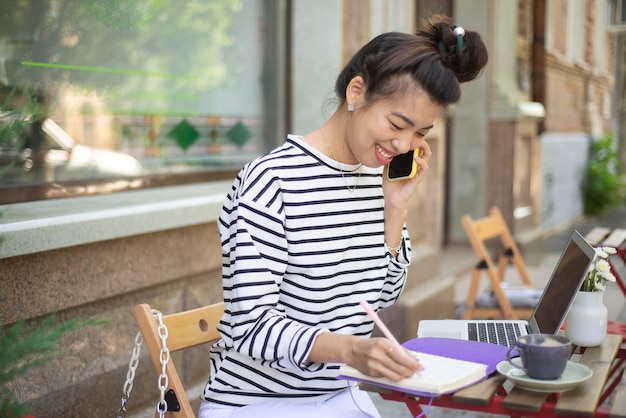 Een freelance meisje werkt op een computer en praat via de mobiele telefoon op een terras