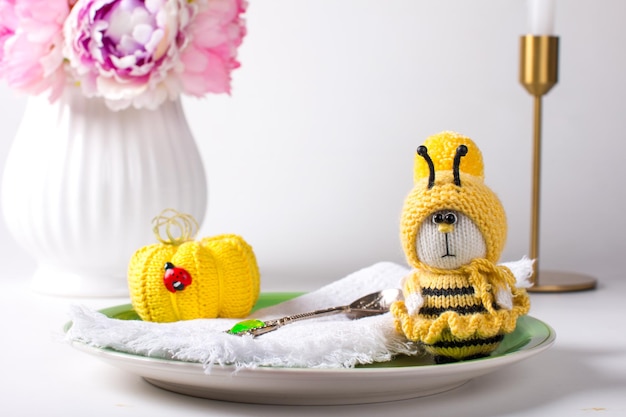Een gebreide gele bij zit op een wit bord met een madeliefje Handgemaakt breispeeltje amigurumi cadeau voor kinderen