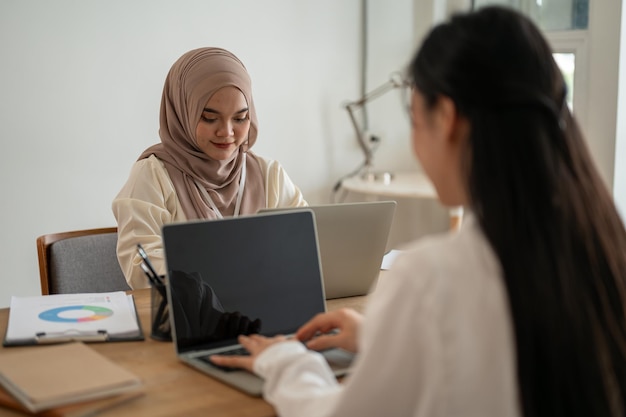 Een geconcentreerde Aziatische moslimzakenvrouw werkt op haar laptop en werkt samen met haar collega