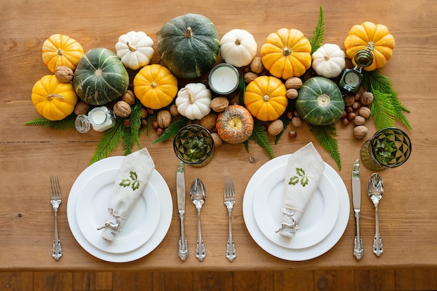 Een gedekte tafel voor twee voor Thanksgiving. Borden, wijnglazen, bestek en selfies op een houten tafel. Tafeldecoratie van pompoenen, noten, kaarsen en jeneverbes bovenaanzicht.