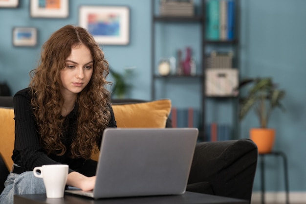 Een gefocuste tiener gebruikt haar laptop terwijl ze thuis op de bank in de woonkamer zit