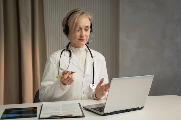 Een gefocuste vrouwelijke arts met een headset met een microfoon raadpleegt een patiënt via een videogesprek