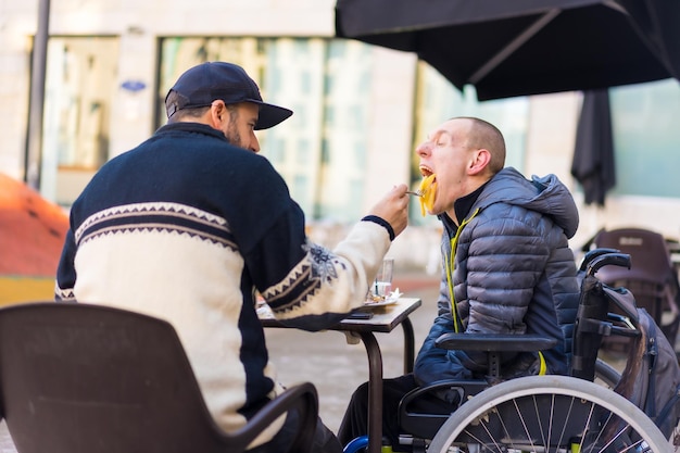 Een gehandicapte eet met de hulp van een familielid op het terras van een restaurant