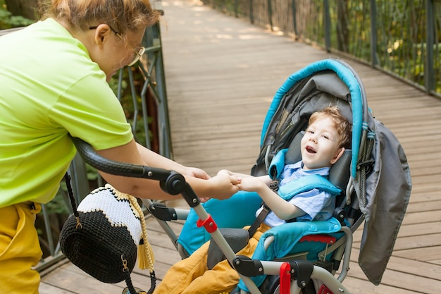 Een gehandicapte jongen in een rolstoel met zijn moeder op straat op een zomerdag. moederliefde en zorg. zachte knuffels.